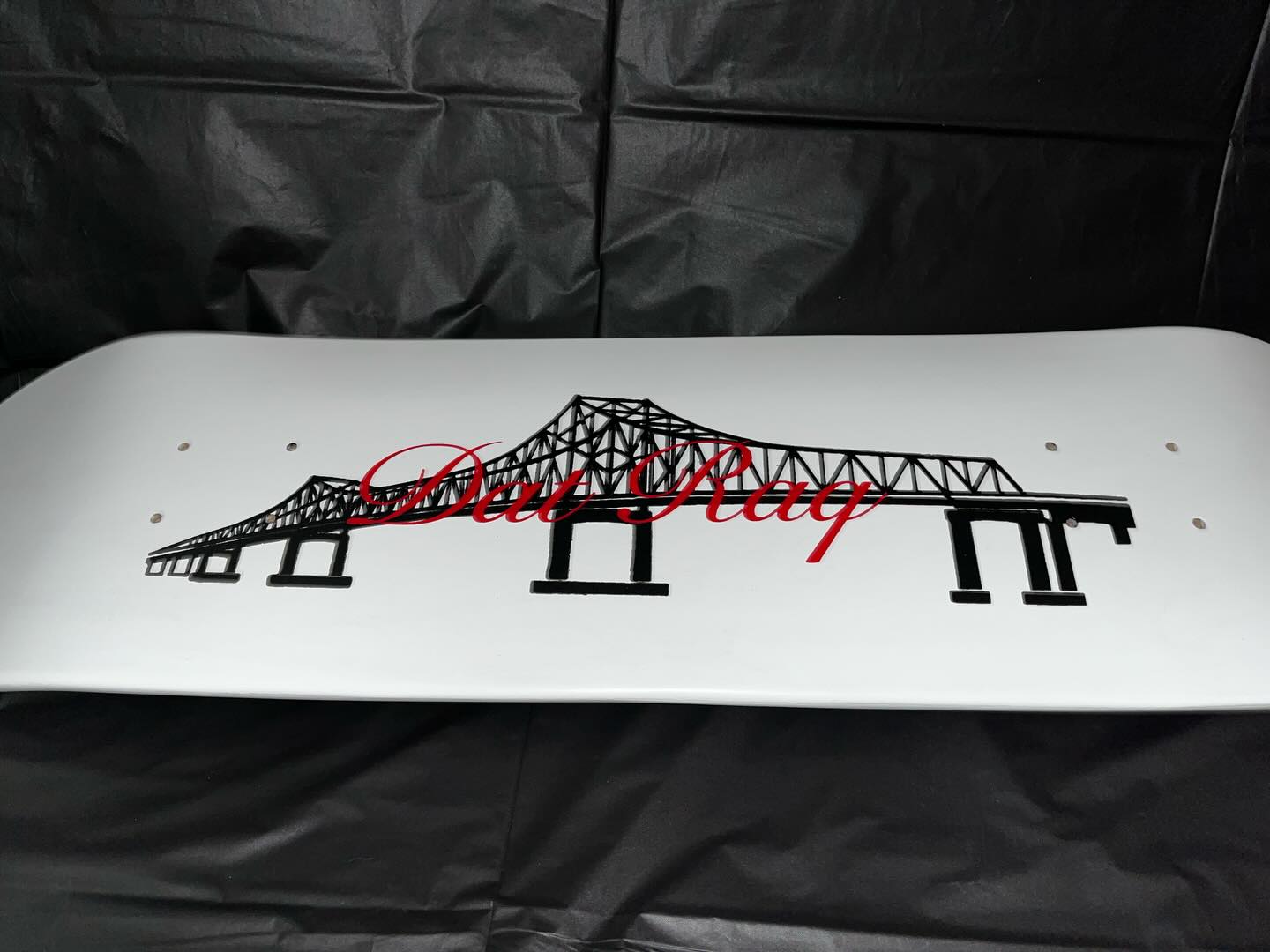 White Dat Raq skate deck with the I-10 Mississippi River bridge graphic and red script