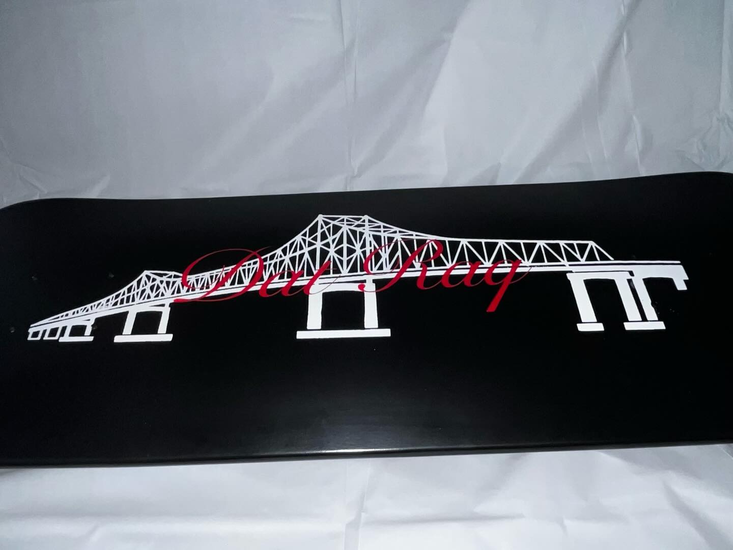 Black Dat Raq skate deck with white I-10 Mississippi River bridge graphic and red script